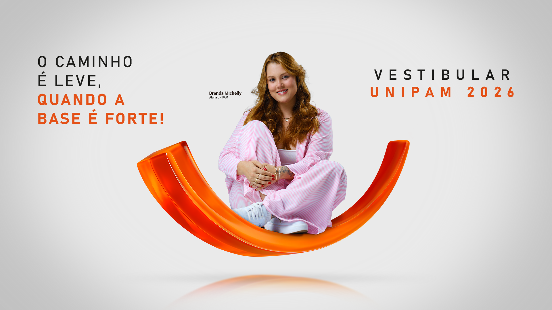 Estudante sorridente sentada sobre uma estrutura curva laranja, vestindo roupa rosa clara. À esquerda, o texto diz: “O caminho é leve, quando a base é forte!”. À direita, aparece “Vestibular UNIPAM 2026” e o nome “Brenda Michelly – Aluna UNIPAM”